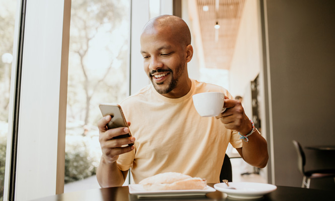 Man drinking coffee at a restaurant and looking at his phone